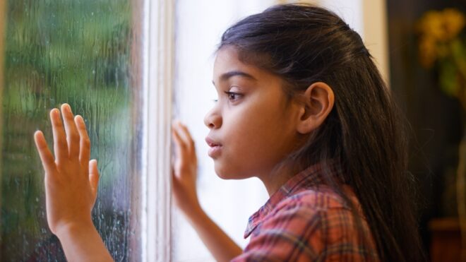 Shot of a cute little girl looking out the window on a rainy day