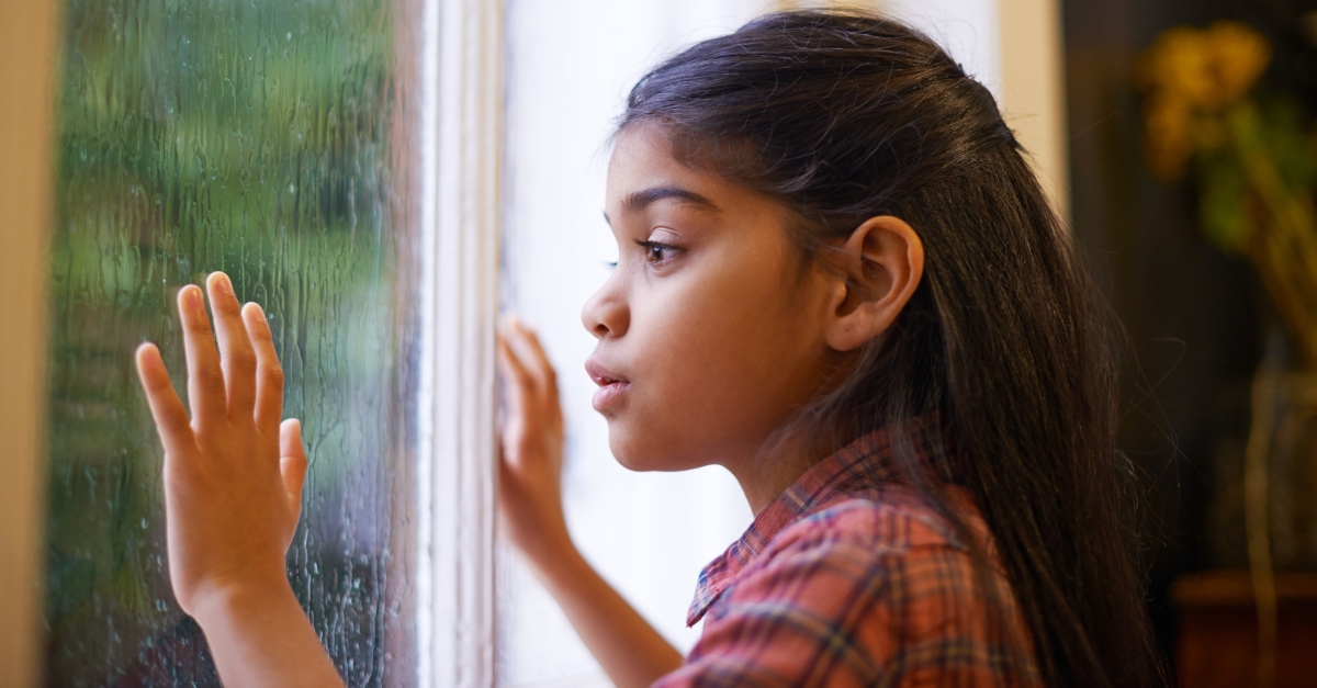 Shot of a cute little girl looking out the window on a rainy day