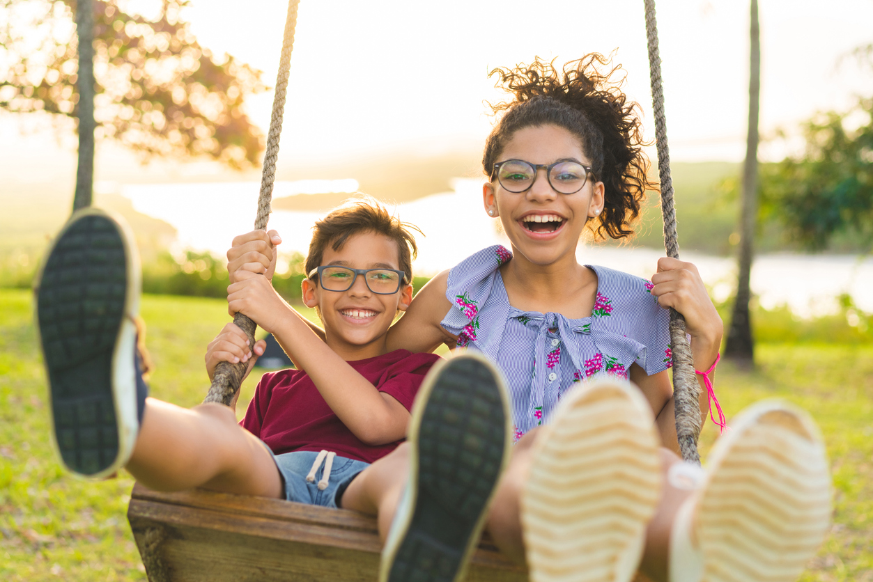 Happy children swinging and smiling at golden sunset