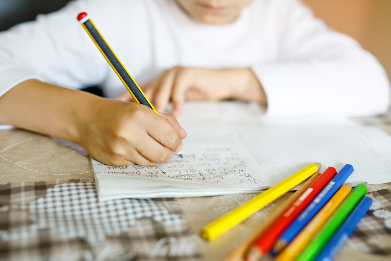 Child doing homework and writing story essay. Elementary or primary school class. Closeup of hands and colorful pencils