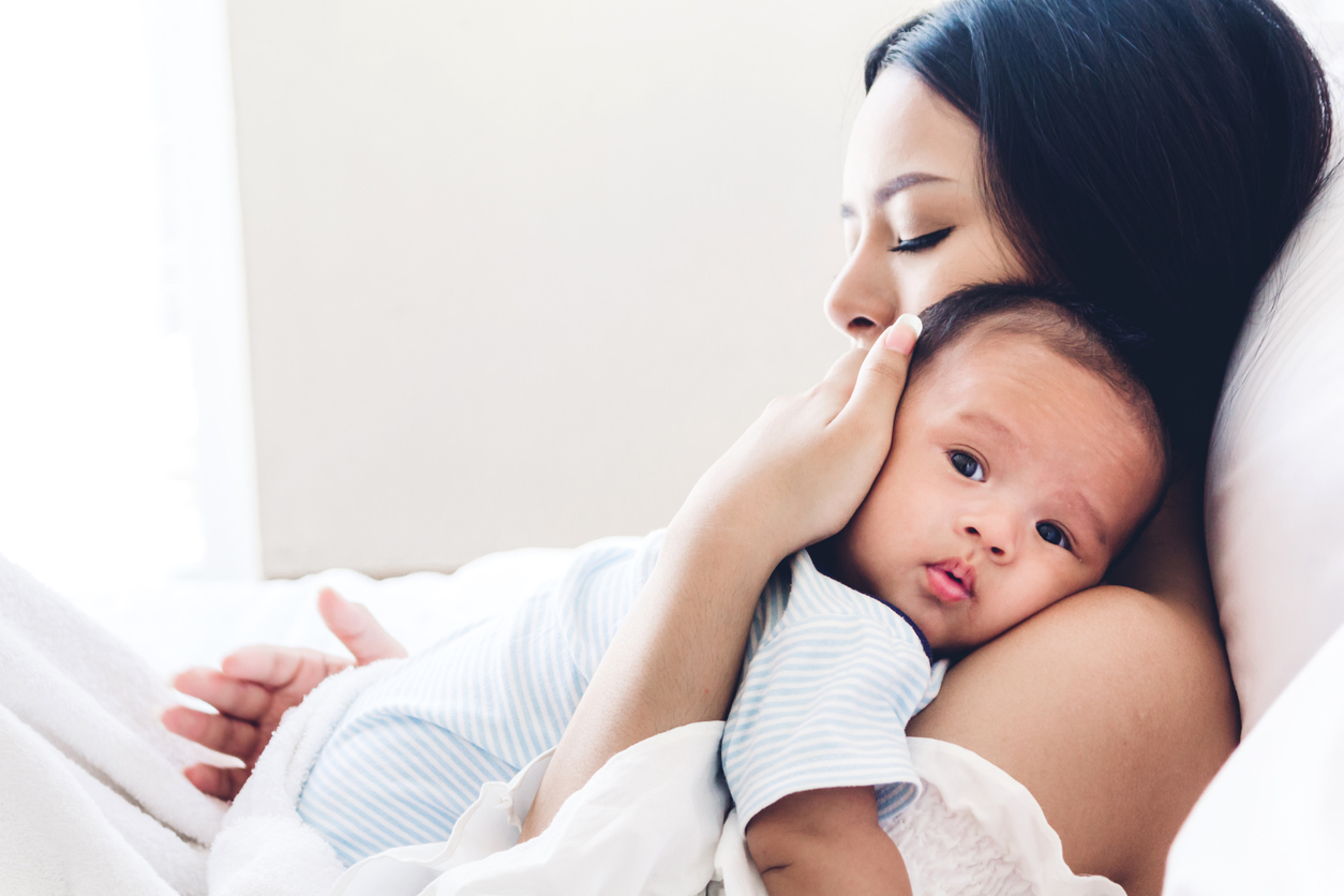 Mother holding baby in her arms and kiss in a white bedroom.Love of family concept
