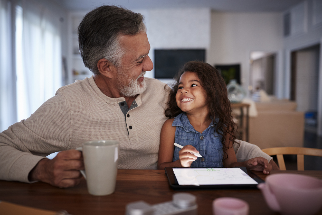 Senior Hispanic man with his granddaughter using tablet computer, looking at each other, front view