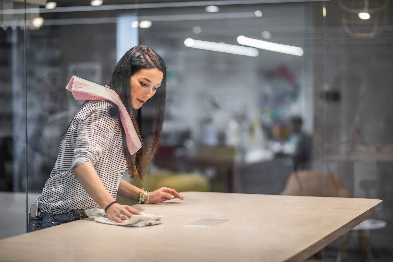 Happy creative woman cleaning the table before a meeting in the office.