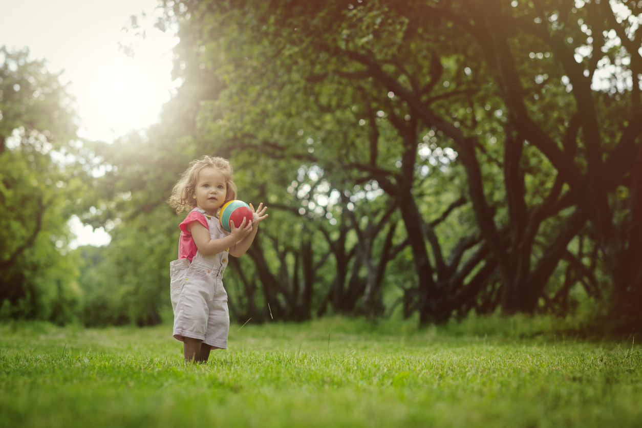 Happy little girl with ball in summer outdoors