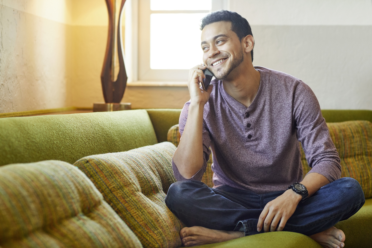 Smiling young man answering smart phone on couch