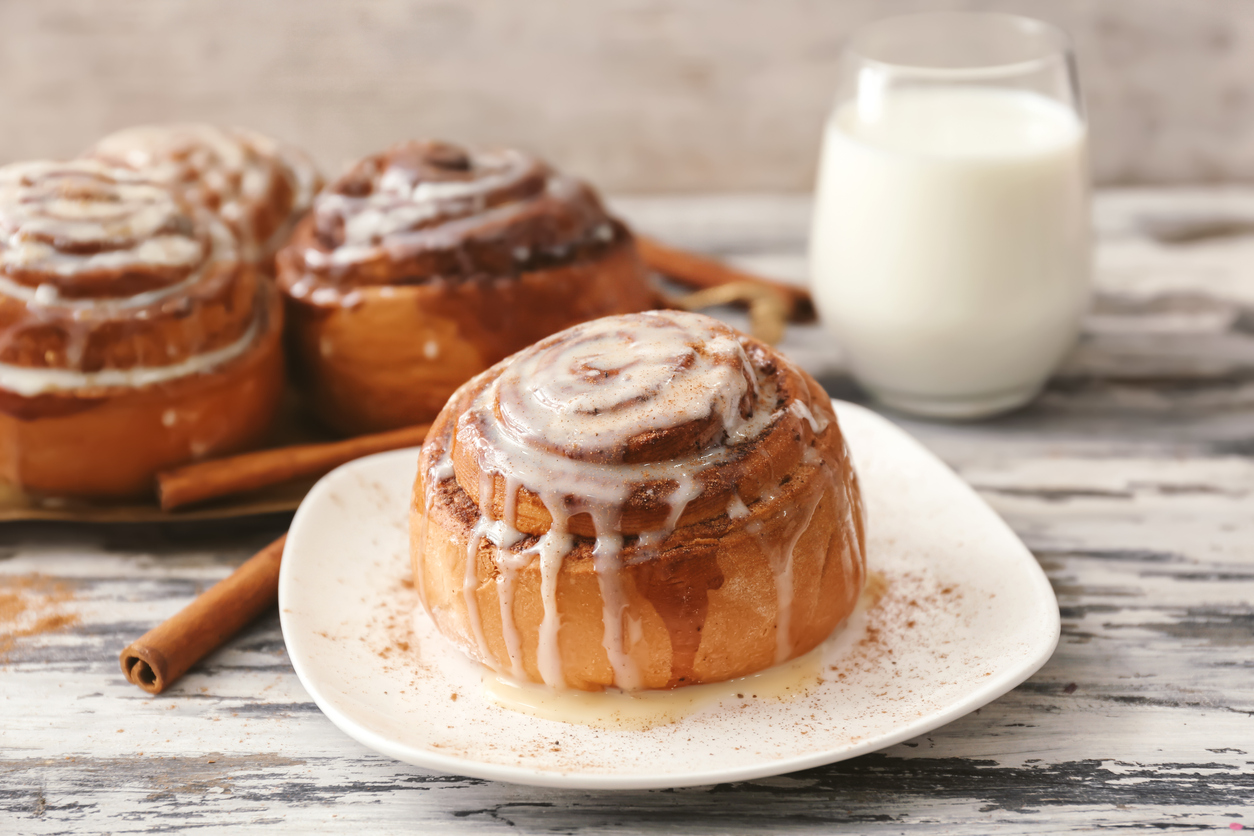 Plate with tasty cinnamon bun on wooden table