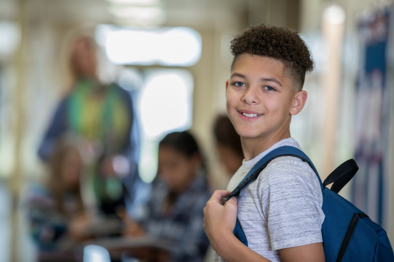 Junior high school boy smiles at the camera while walking to class in hallway
