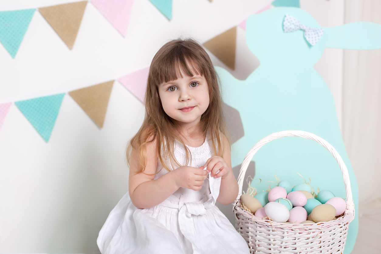 Easter 2019 Beautiful little girl in a white dress with Easter eggs and a basket. Big Easter eggs and bunnies, colorful place. A lot of different colorful Easter eggs. Multicolored flag, decor