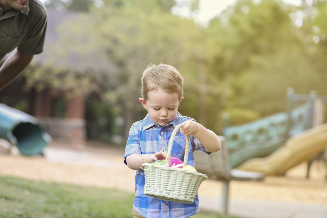 Little boy with basket hunting Easter eggs at park.