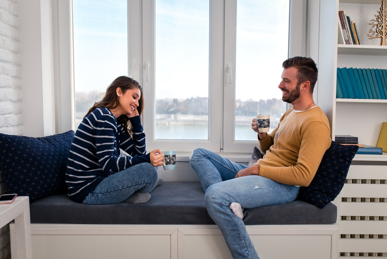 Loving couple sitting together by the window in the apartment and drinking coffee in the morning.