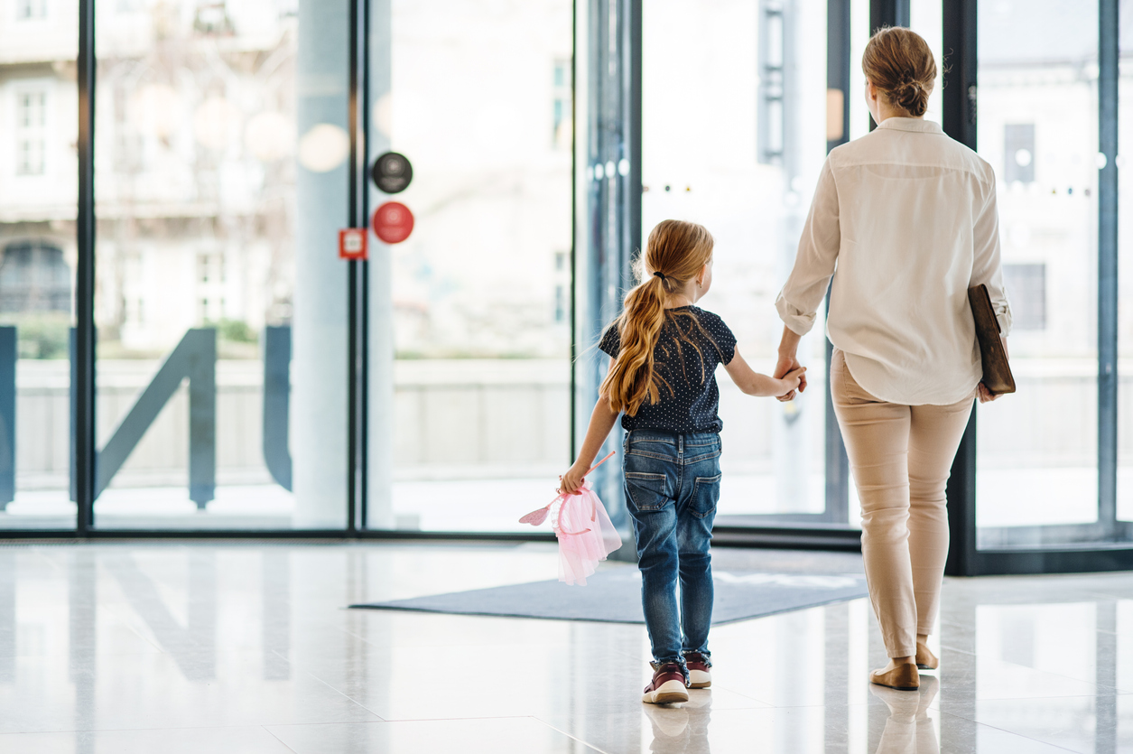 A rear view of businesswoman with small daughter walking in office building.