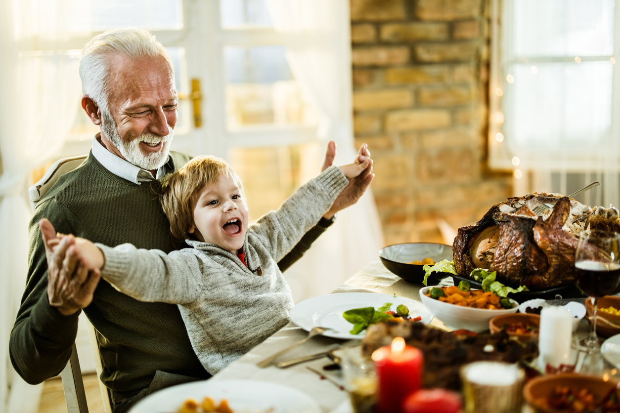 Happy grandfather and grandson having fun during Thanksgiving lunch at home.