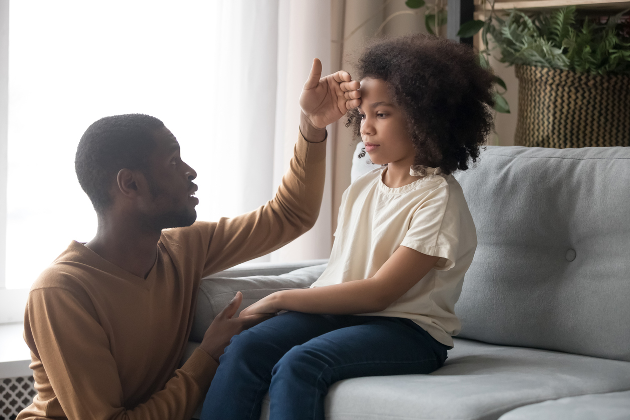 Worried father touch forehead of unhealthy daughter sitting on sofa