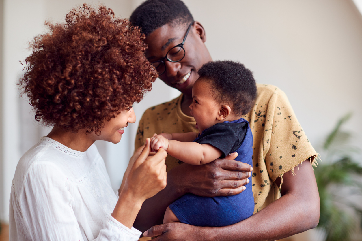 Loving Parents Playing With Newborn Baby At Home In Loft Apartment