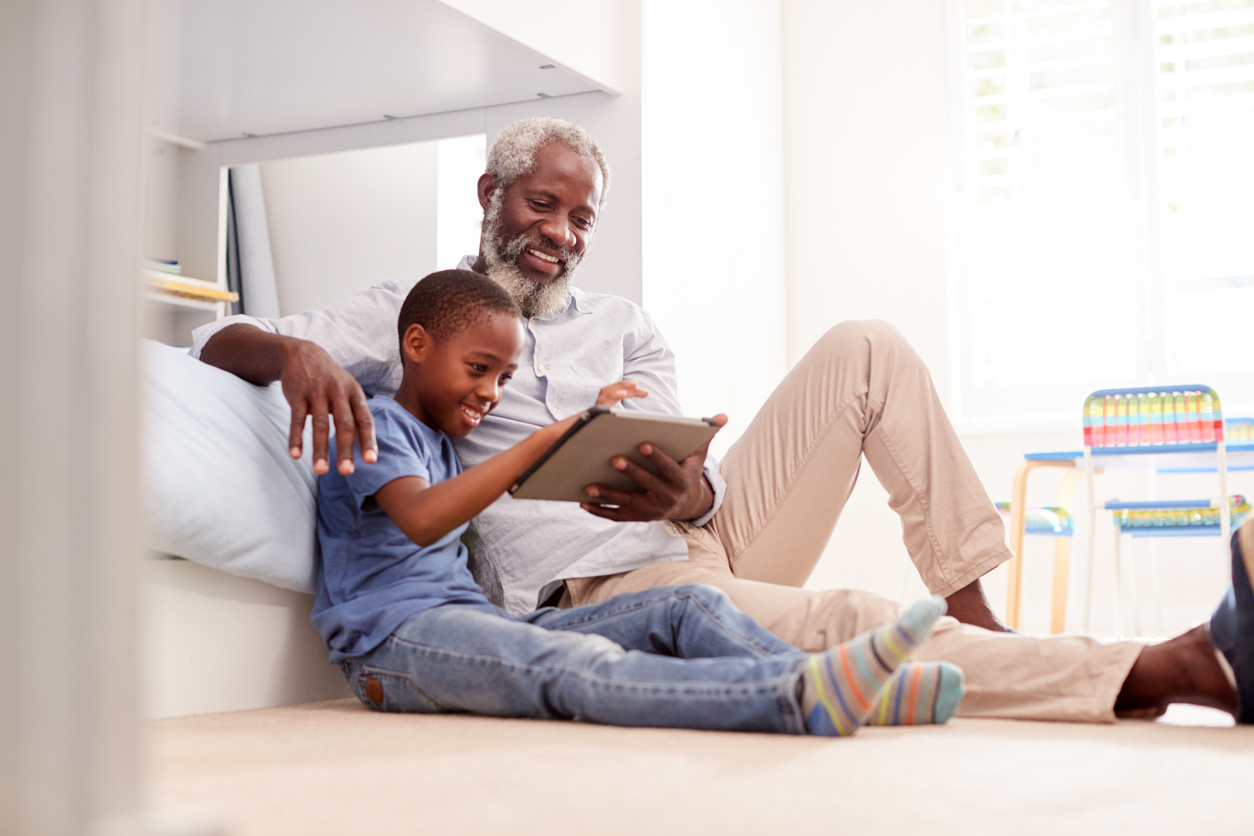 Grandfather Sitting With Grandson In Childs Bedroom Using Digital Tablet Together