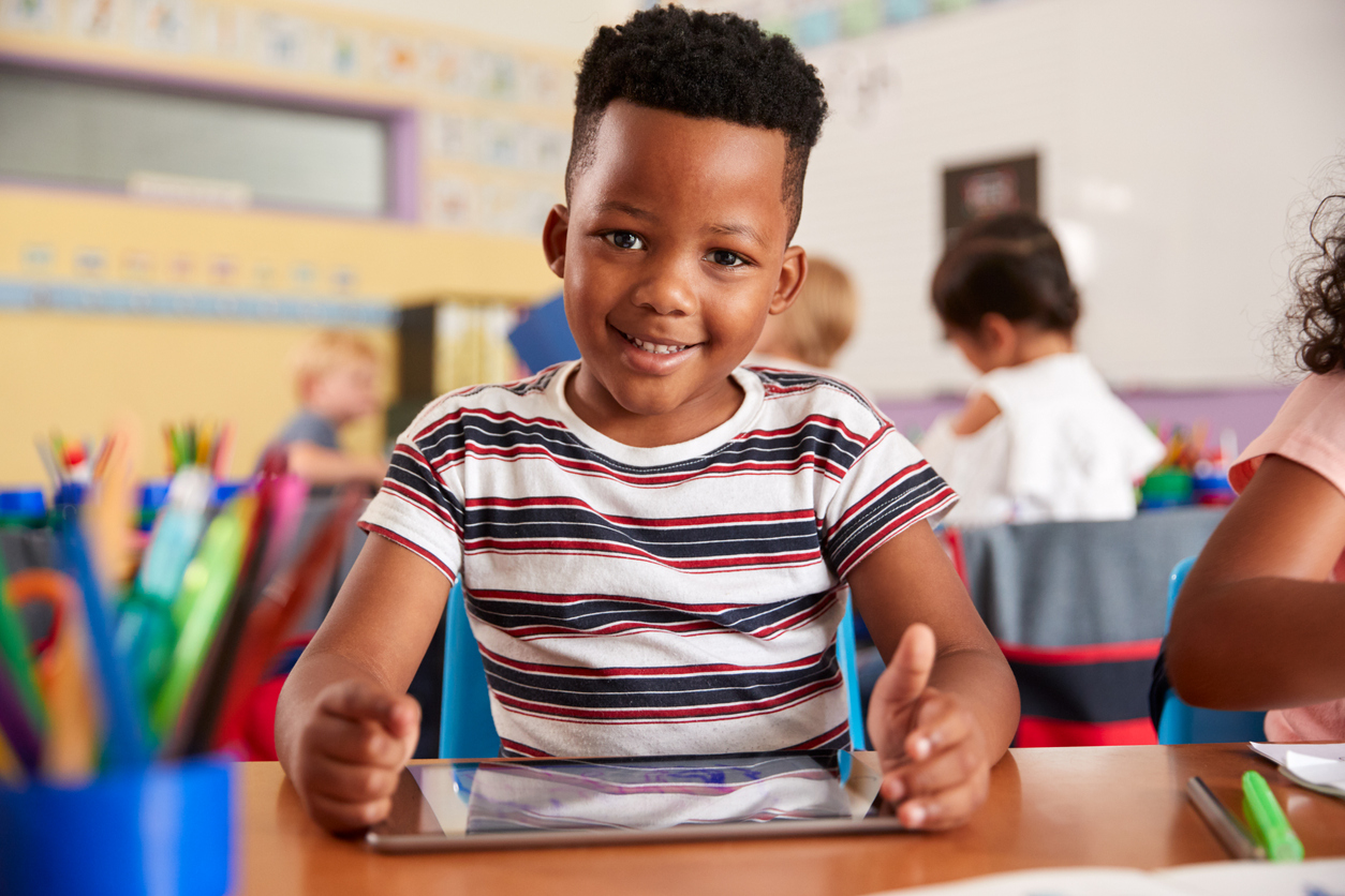 Portrait Of Male Pupil In Elementary School Drawing Using Digital Tablet In Classroom