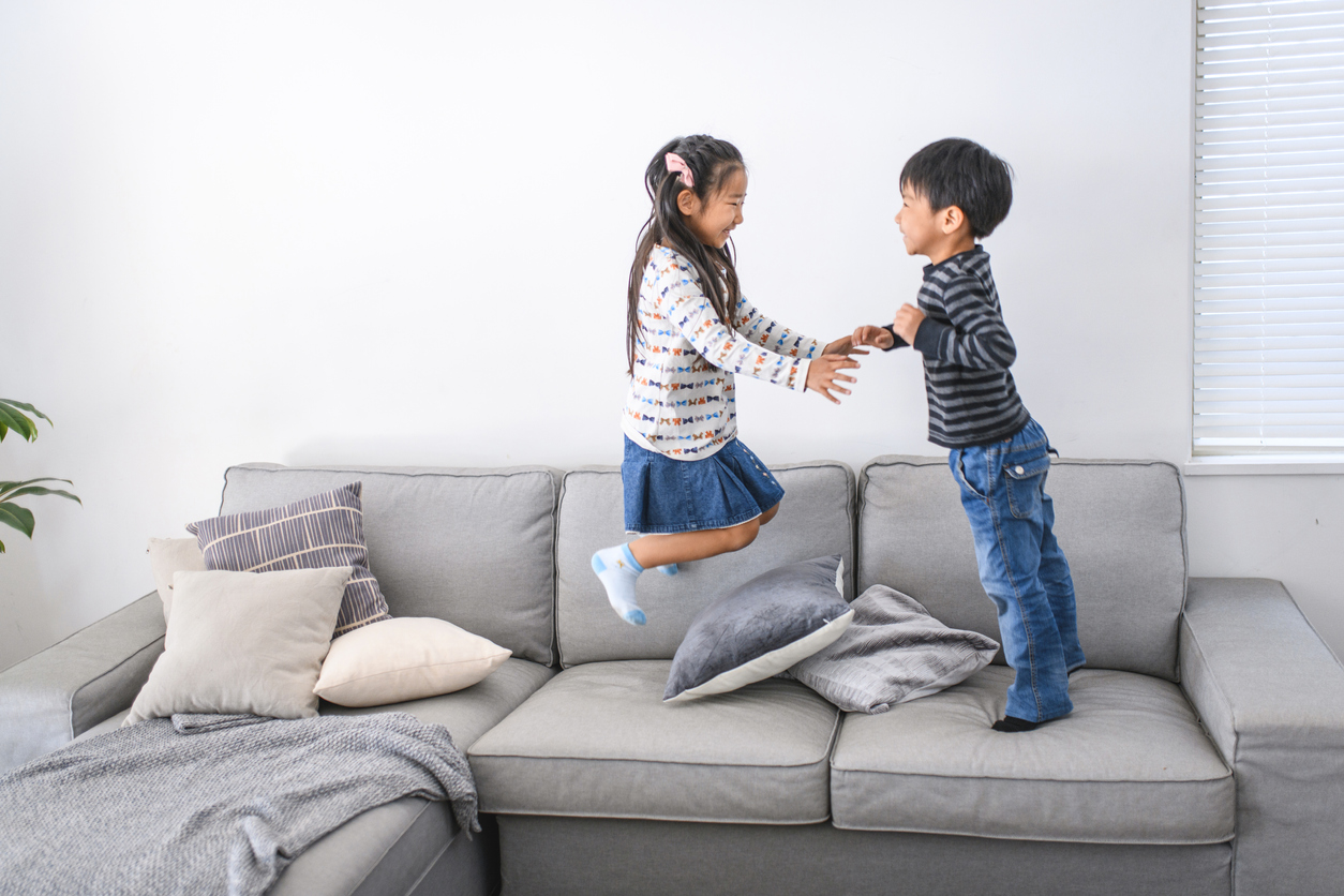 Playful Young Japanese Siblings Jumping on Sofa