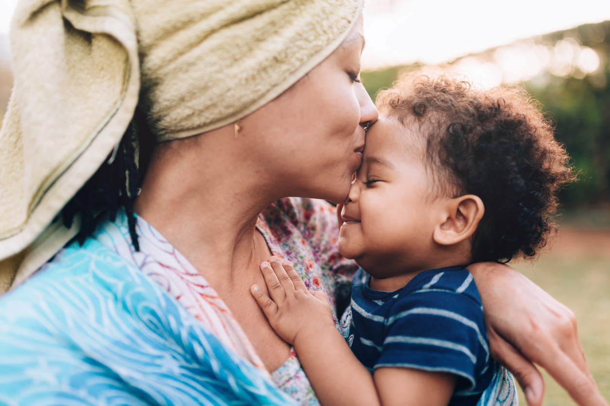 Young African descendant mother kissing her baby son on the forehead