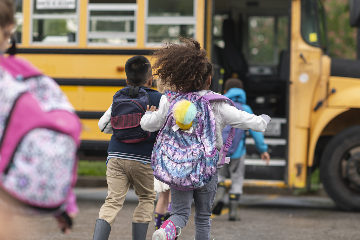 Diverse group of happy children getting on school bus