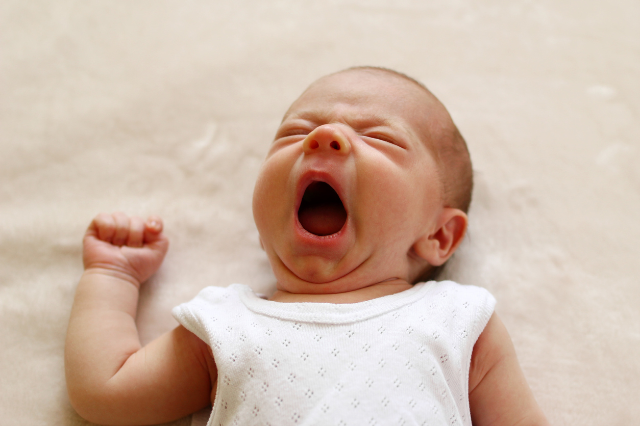 One month child is yawning lying on a blanket before go to sleep.