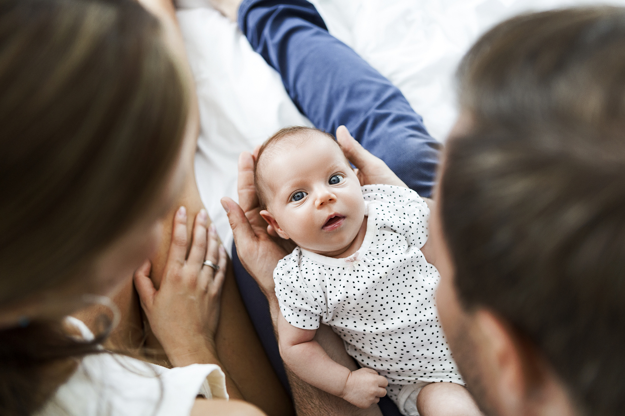 Mother ,father and baby child on a white bed playing