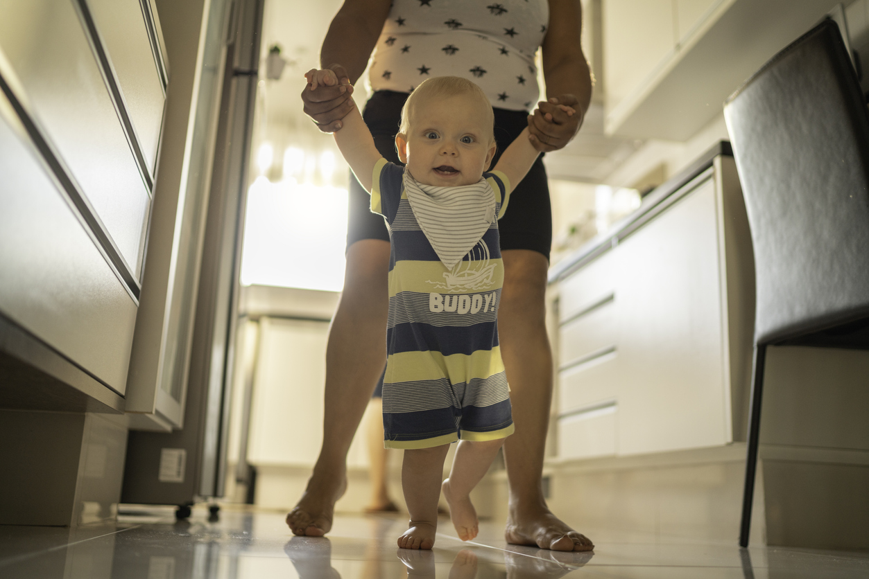 Babysitter helping baby boy learn to walk at home