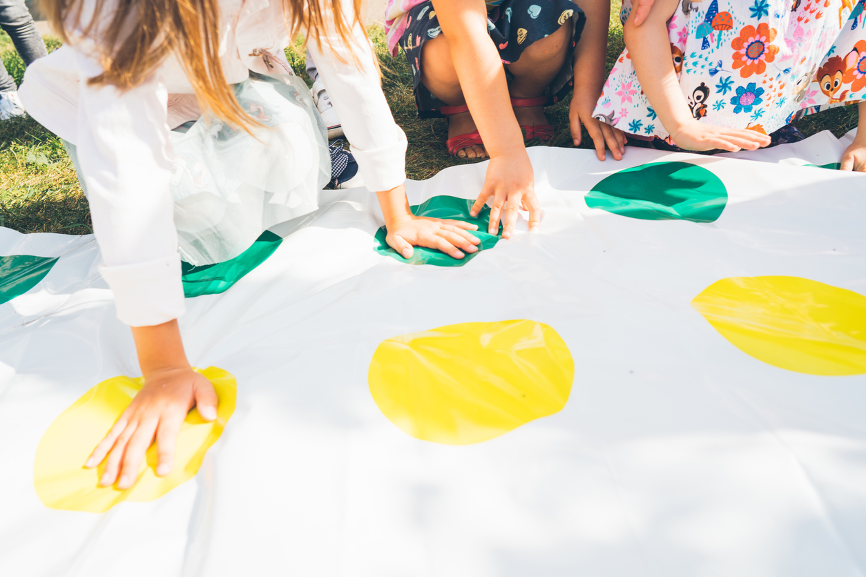 Children play a twister on the grass. Hands on yellow.