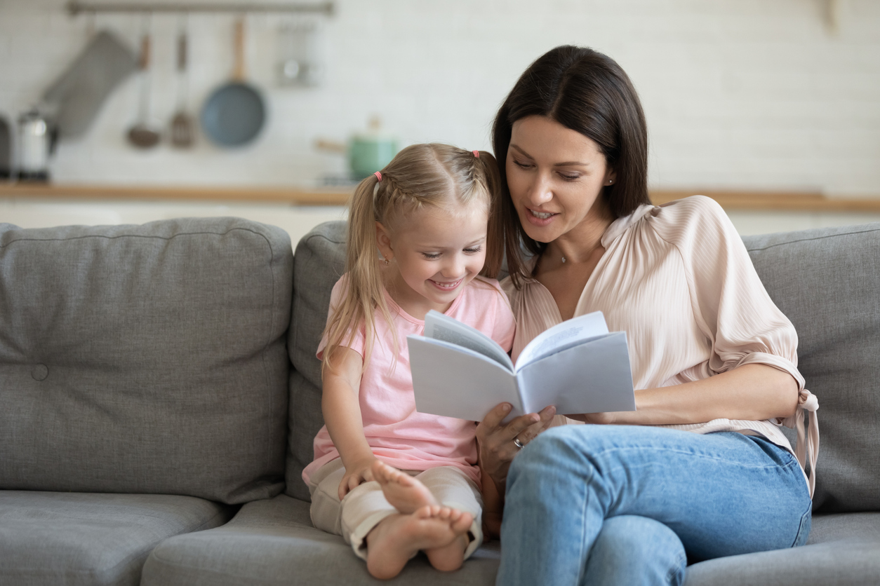 Happy mother and little daughter reading book together at home