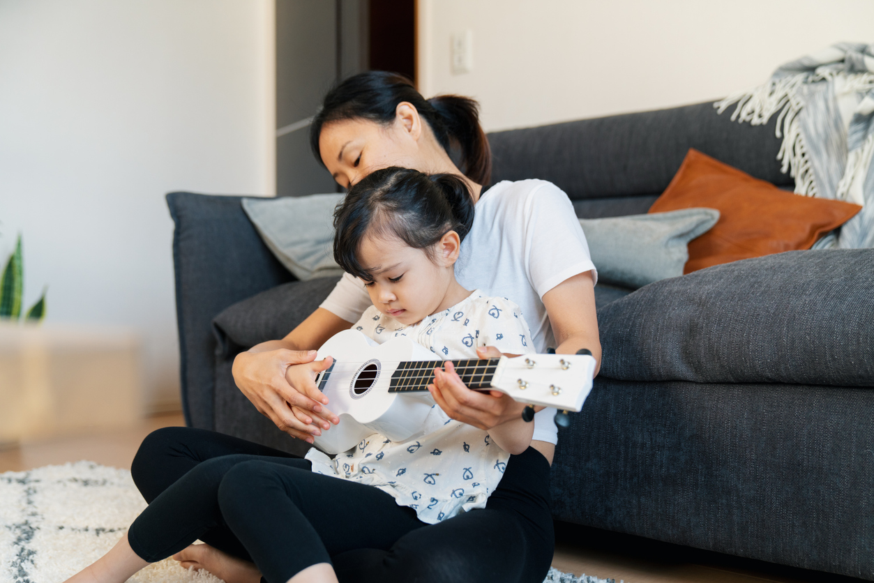 Mother teaching daughter to play ukulele at home