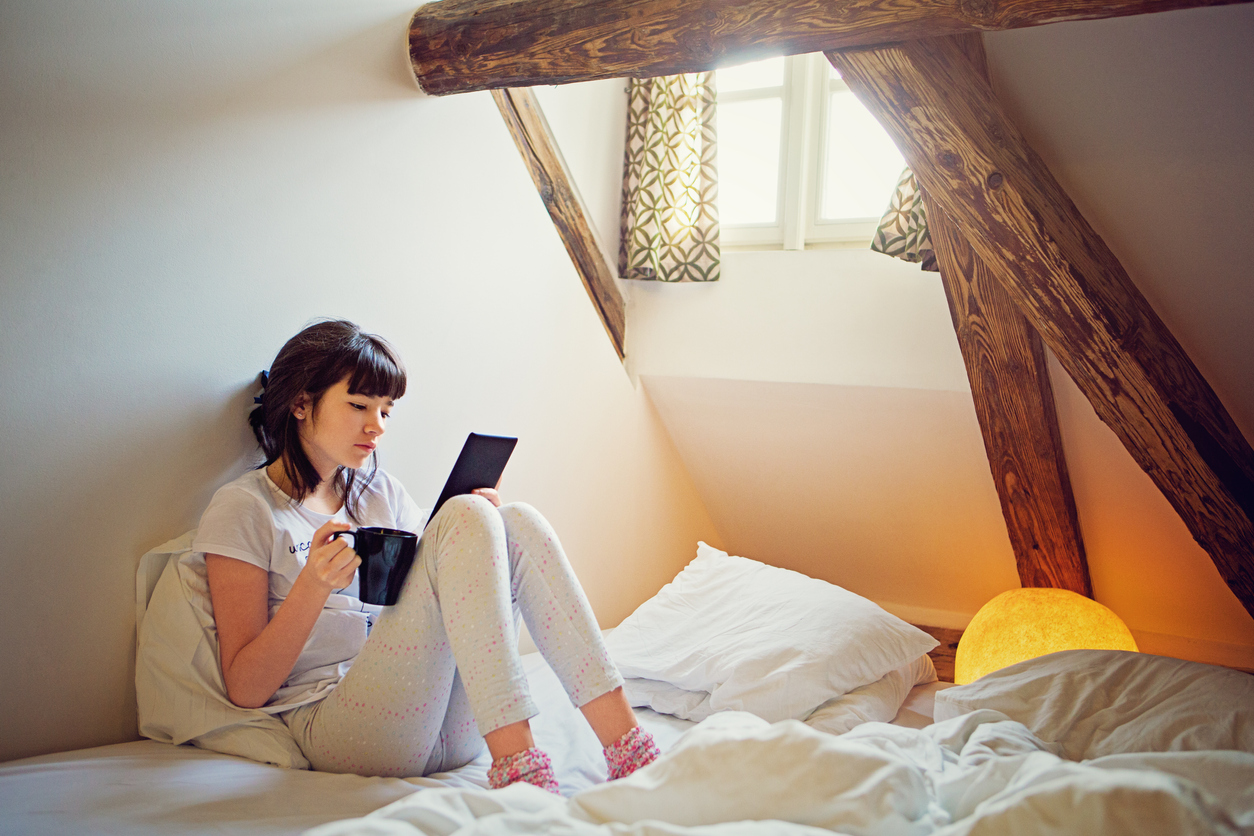 Young teenage girl is reading ebook in her bed