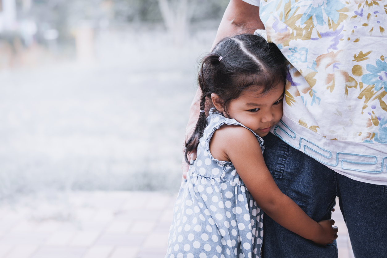 Sad asian little girl hugging her mother leg