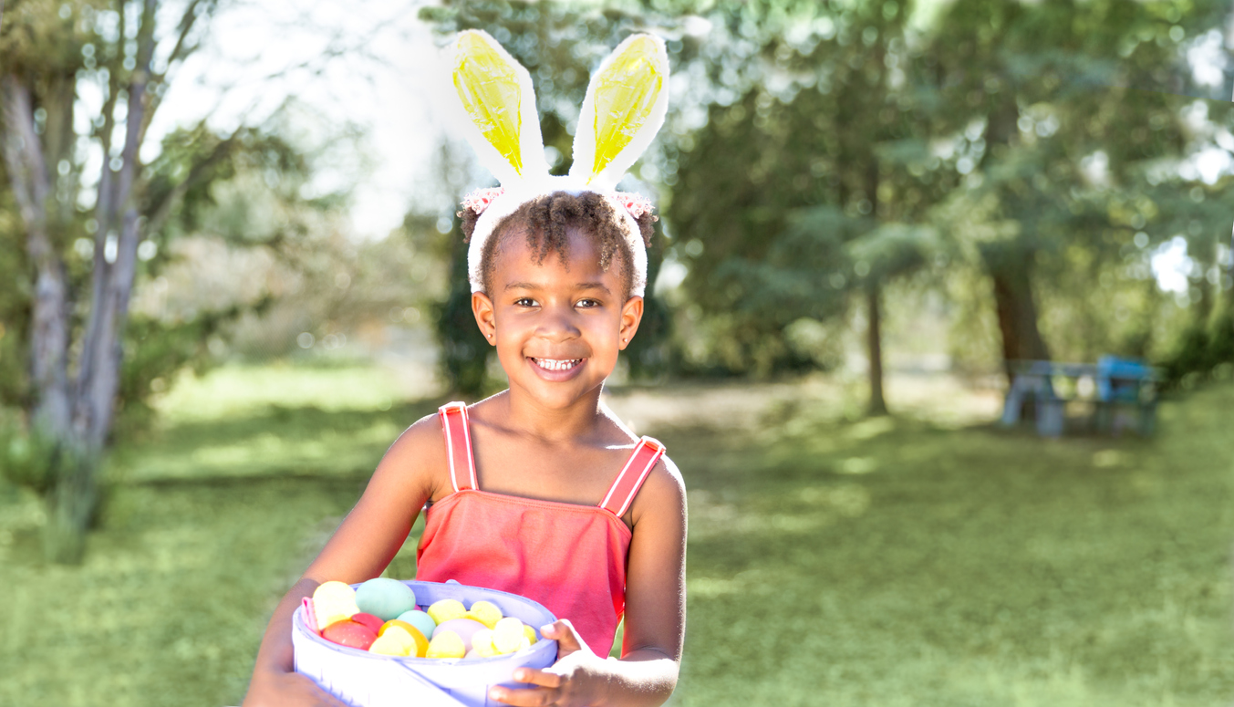 Cute African American girl wearing bunny ears, holding Easter basket with eggs.