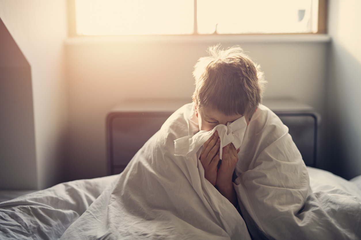 Sick little boy lying in bed and blowing nose