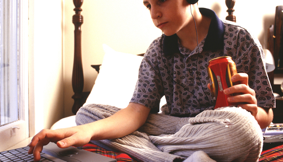 Teenage boy (16-17) using laptop, sitting on bed