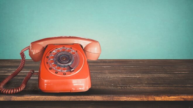 Old retro red telephone on table with vintage green pastel background