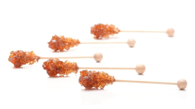 Brown sugar crystal on wooden stick isolated over white background