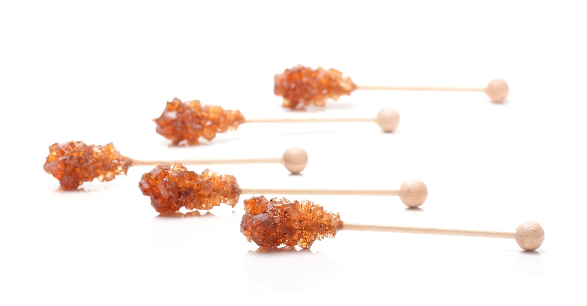 Brown sugar crystal on wooden stick isolated over white background