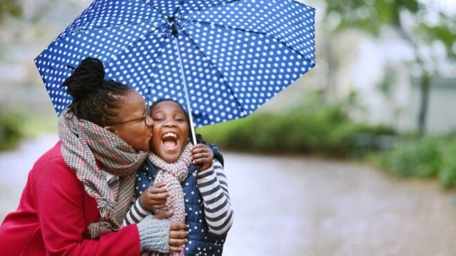 Shot of woman kissing her daughter under an umbrella