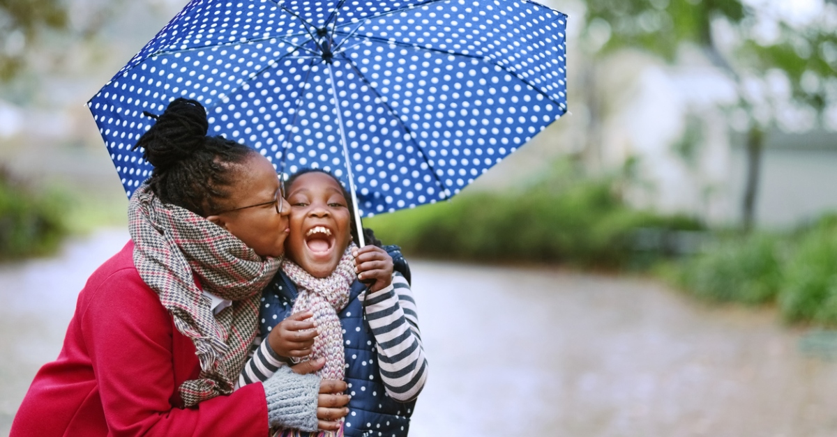 Shot of woman kissing her daughter under an umbrella