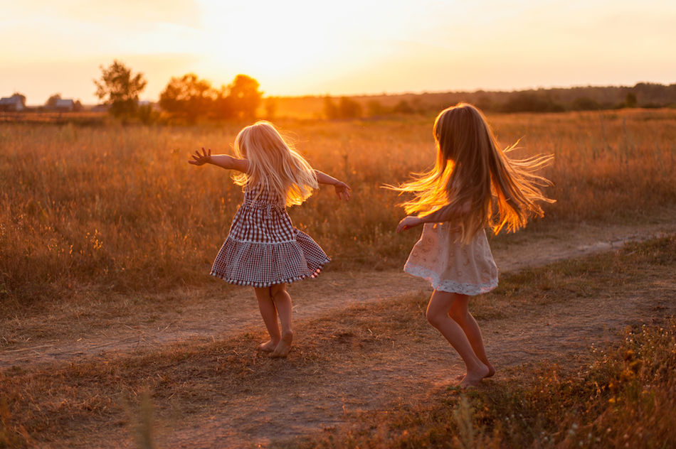 two girls dancing in a field at sunset