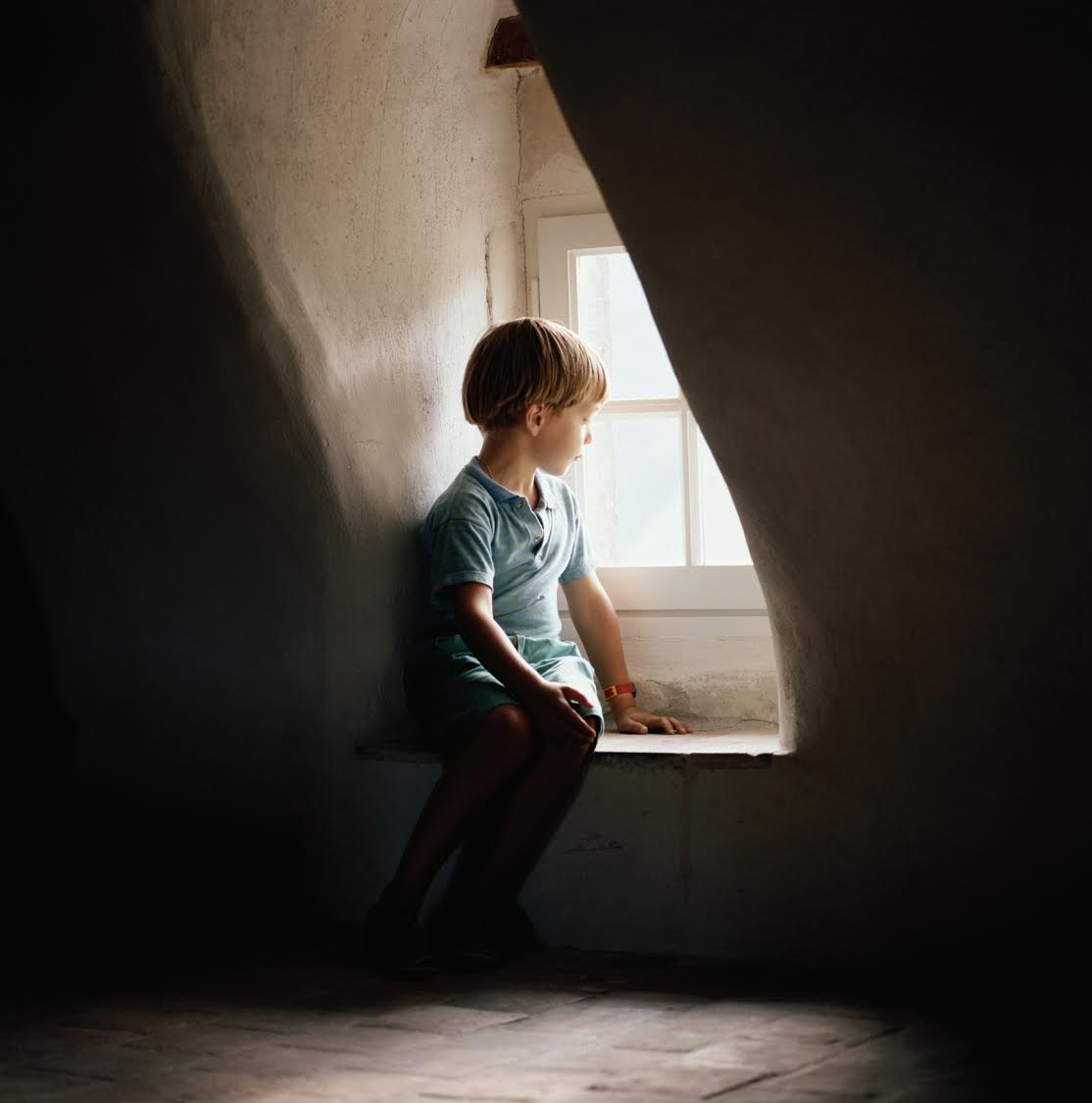 Boy (6-7) sitting on window sill, looking out window