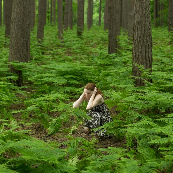 Young woman crouching in forest with head in hands