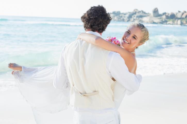 Handsome groom carrying his beautiful wife smiling at camera