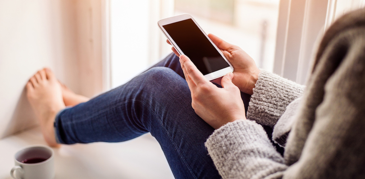 Unrecognizable woman sitting on window sill with smart phone