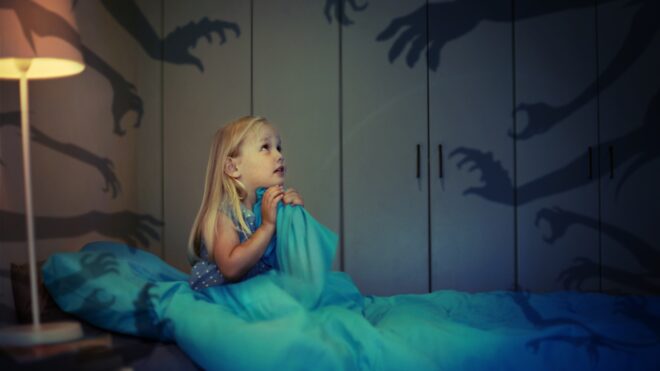 Little girl in bed surrounded by scary shadows