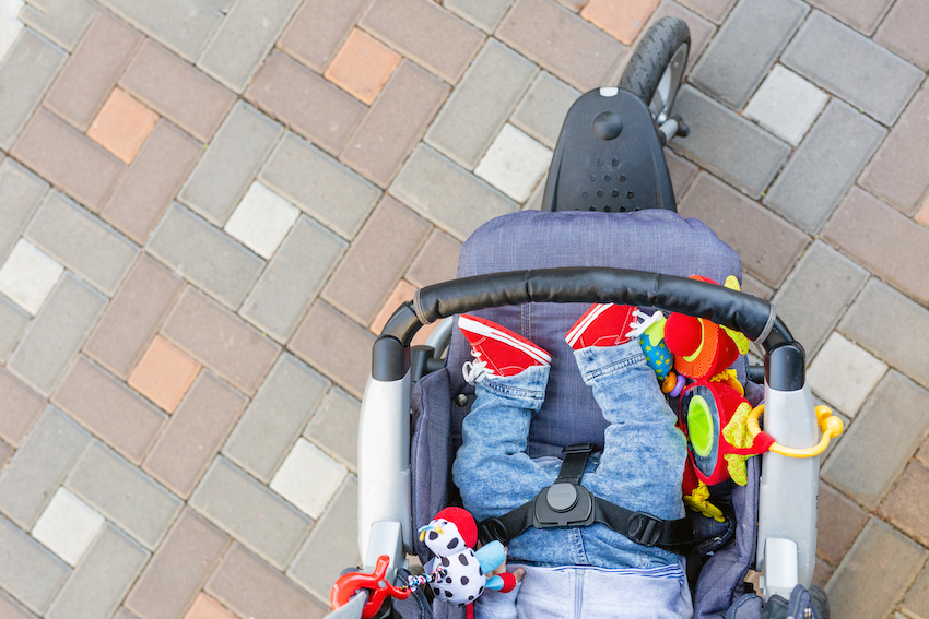 Baby sleeping three-wheel stroller outdoor. Child in bright casual costume lying at big comfortable pram. Parent walking with carriage in city park. View from above