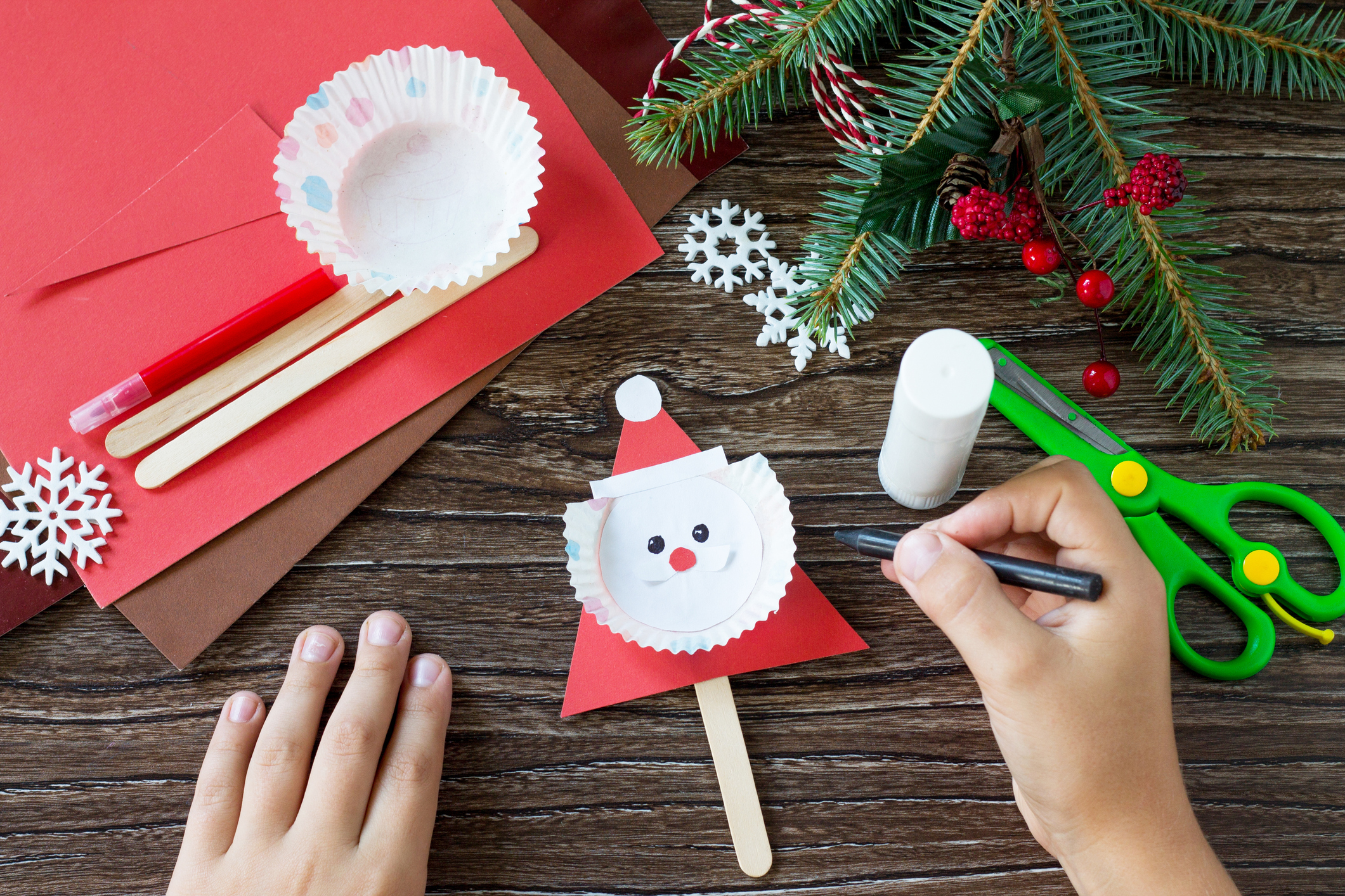 The child draws details Christmas Santa stics puppets. Handmade. Project of children's creativity, handicrafts, crafts for kids.