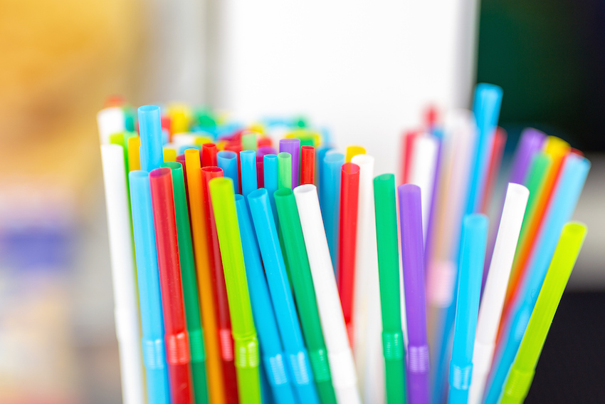 Bunch of colorful plastic sipping straws in wooden box at cafe counter. Drinks decoration and accessories. Bright multicolored background