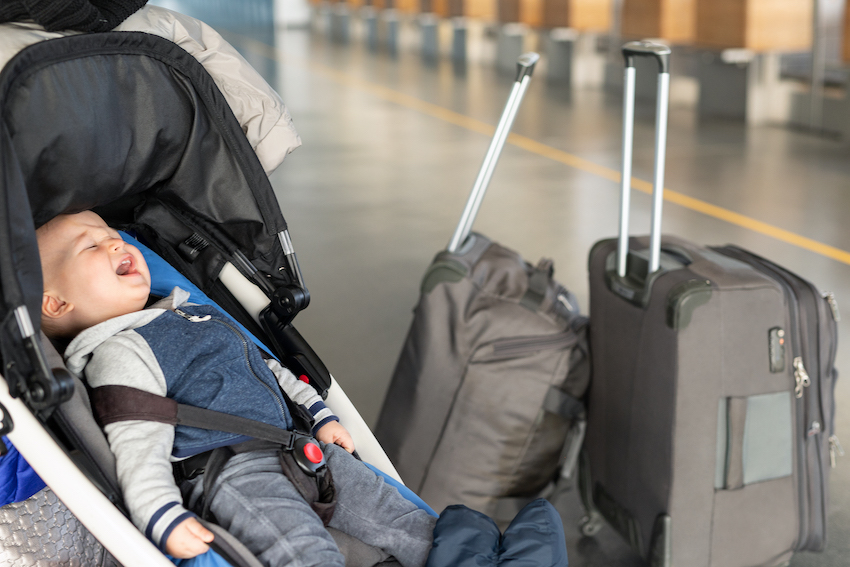 Screaming baby boy sitting in stroller near luggage at airport terminal. Child in carriage near check-in desk counter. Children tears , panic and hysterics. Travelling with small children concept