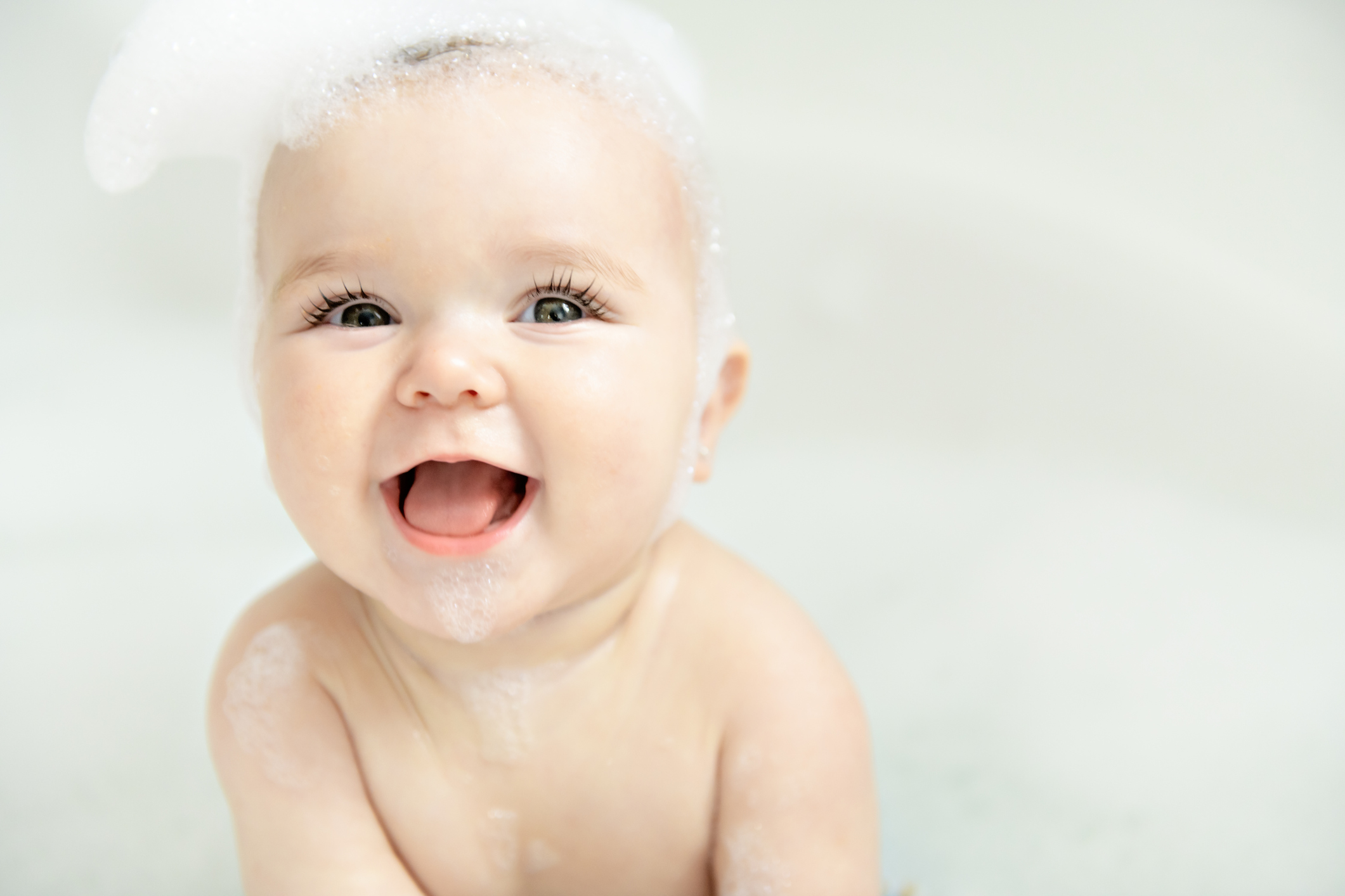 A Baby girl bathes in a bath with foam and soap bubbles